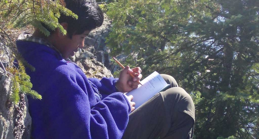 A person rests agains a rock while journaling. 
